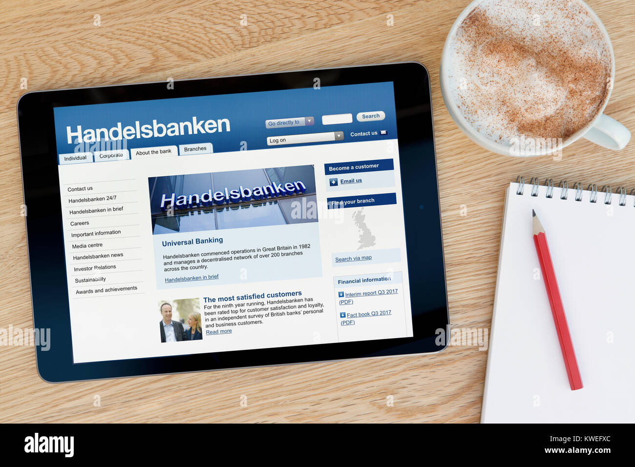 Die Handelsbanken Website auf einem iPad tablet device, ruht auf einem hölzernen Tisch neben einem Notizblock, Bleistift und Tasse Kaffee (nur redaktionell) Stockfoto