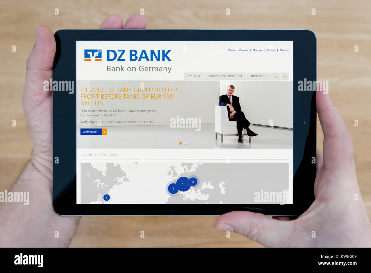 Ein Mann schaut auf die DZ Bank Website auf seinem iPad tablet device, Schuß gegen einen hölzernen Tisch top Hintergrund (nur redaktionelle Nutzung) Stockfoto