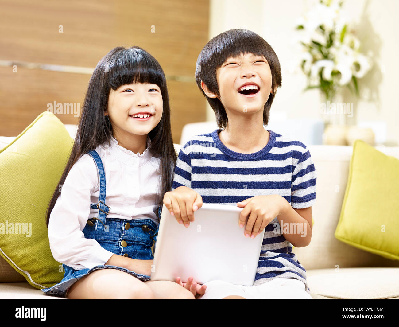 Zwei süße asiatische Kinder Jungen und Mädchen sitzen auf der Couch halten Digitale tablet Lachen. Stockfoto