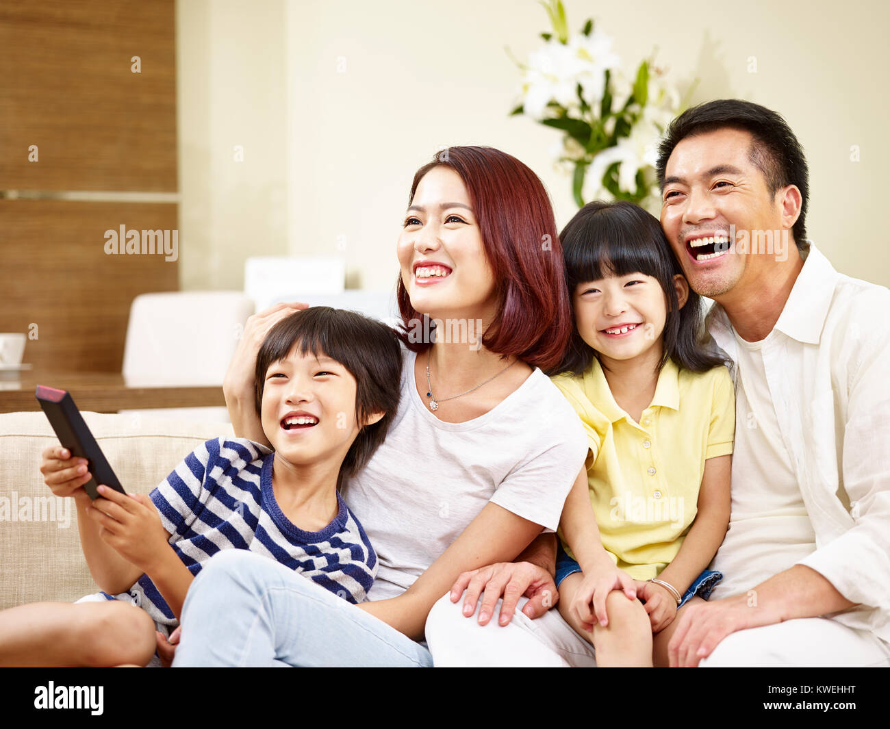 Gerne asiatische Familie mit zwei Kindern sitzt auf der Couch zu Hause vor dem Fernseher. Stockfoto