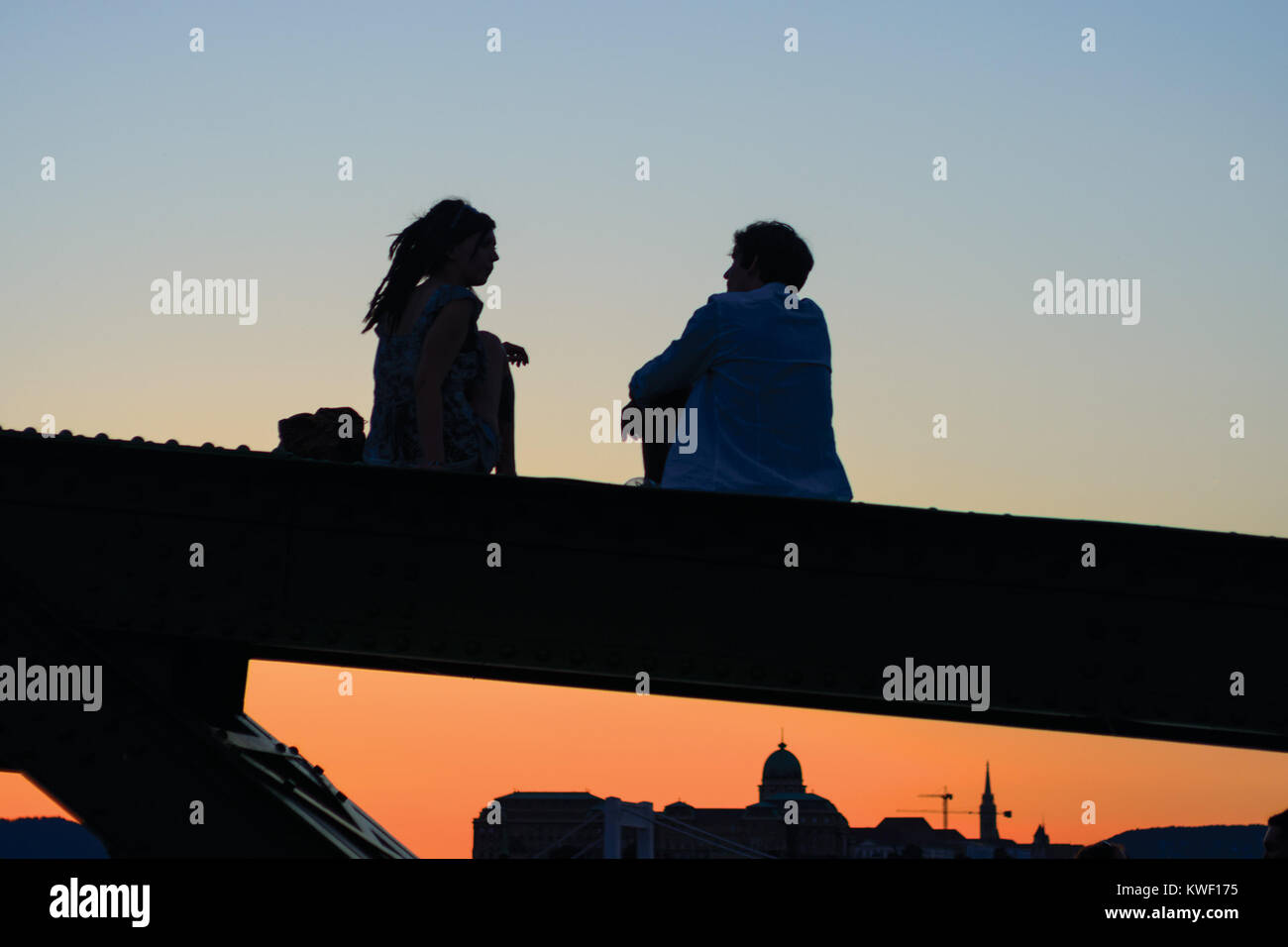 Silhouetten von junges Paar sitzt und spricht auf Brücke Strahl Stockfoto