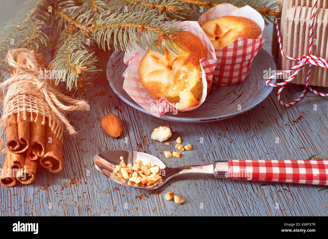 Lemon mini Muffins mit Blumenschmuck in rot-weißem Papier auf rustikalen Holztisch mit Weihnachten Zweige, Mandeln und Zimtstangen. Bild gefiltert. Stockfoto
