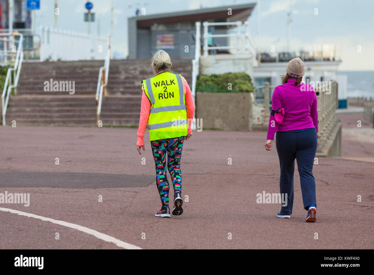 Zwei Frau zu Fuß entlang der Promenade hastings Hi-vis Jacke gehen 2 run bewölkten Tag, East Sussex Stockfoto