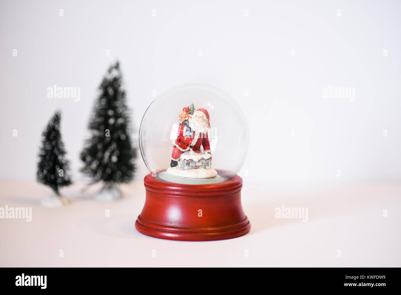 Eine Szene mit einem roten Schneekugel mit Santa Clause Abstieg der Schornstein Holding seinen Sack mit Geschenken und Weihnachtsbäume Stockfoto