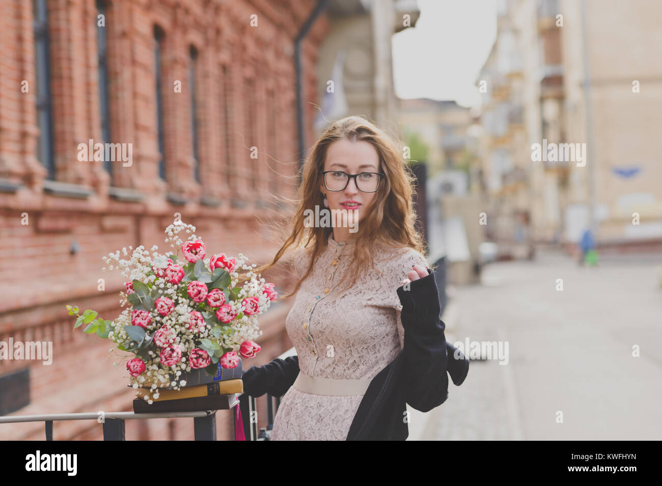Ein glückliches Mädchen in Lacy Kleid mit einem Blumenstrauß und einer Packung der Bücher in der Nähe ein altes Gebäude Stockfoto