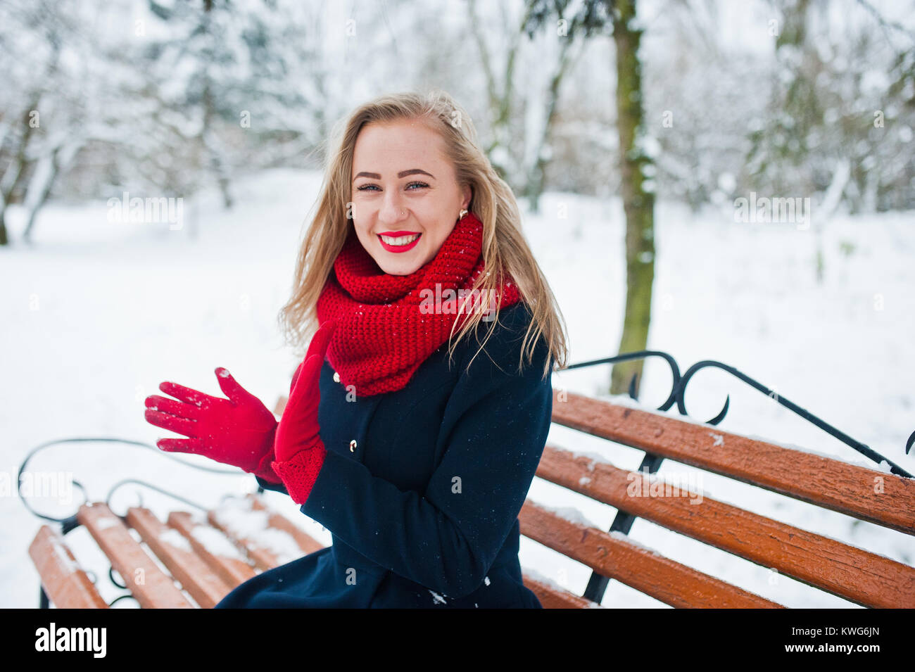 Blonde Mädchen in roten Schal und Mantel sitzen an der Werkbank von der winterlichen Tag. Stockfoto