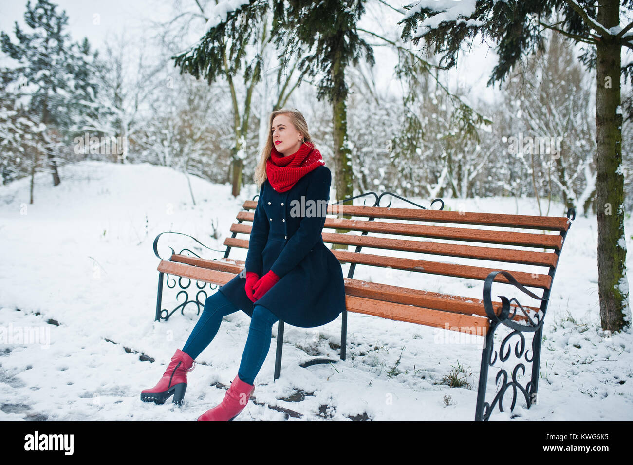 Blonde Mädchen in roten Schal und Mantel sitzen an der Werkbank von der winterlichen Tag. Stockfoto