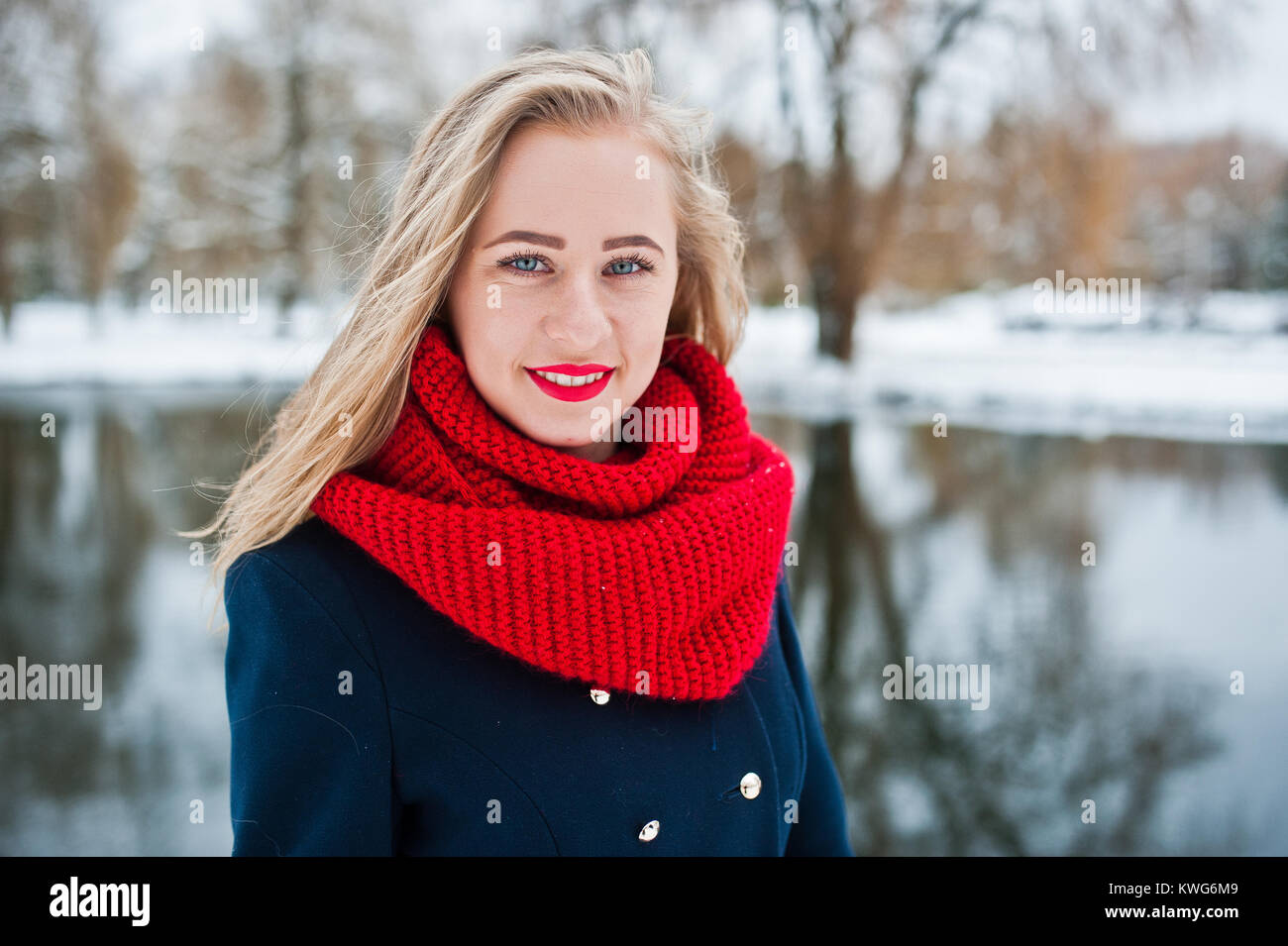 Portrai des blonden Mädchen in roten Schal und Mantel gegen zugefrorenen See im Winter Tag. Stockfoto