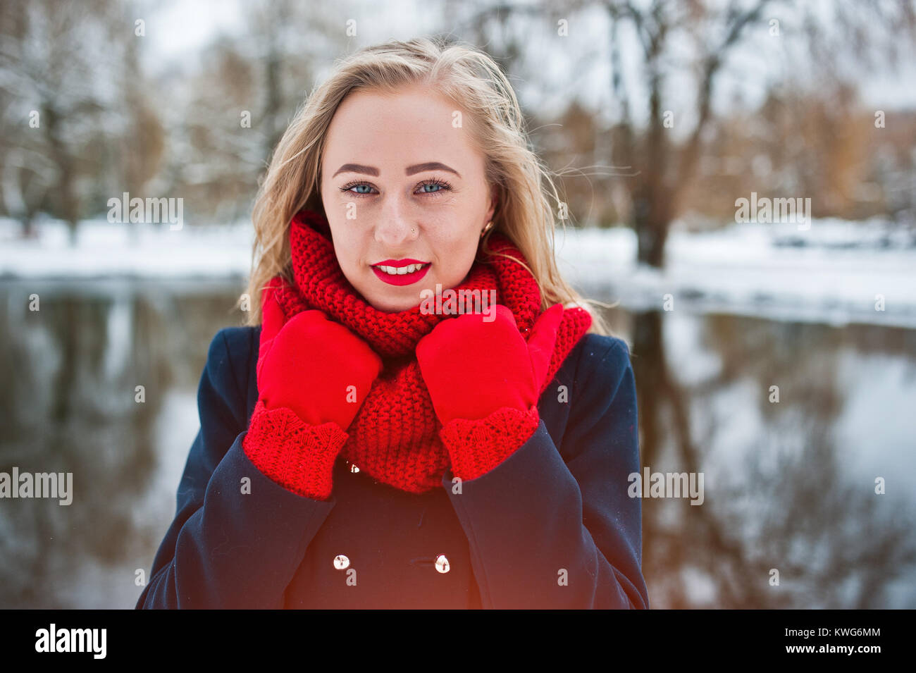 Portrai des blonden Mädchen in roten Schal und Mantel gegen zugefrorenen See im Winter Tag. Stockfoto
