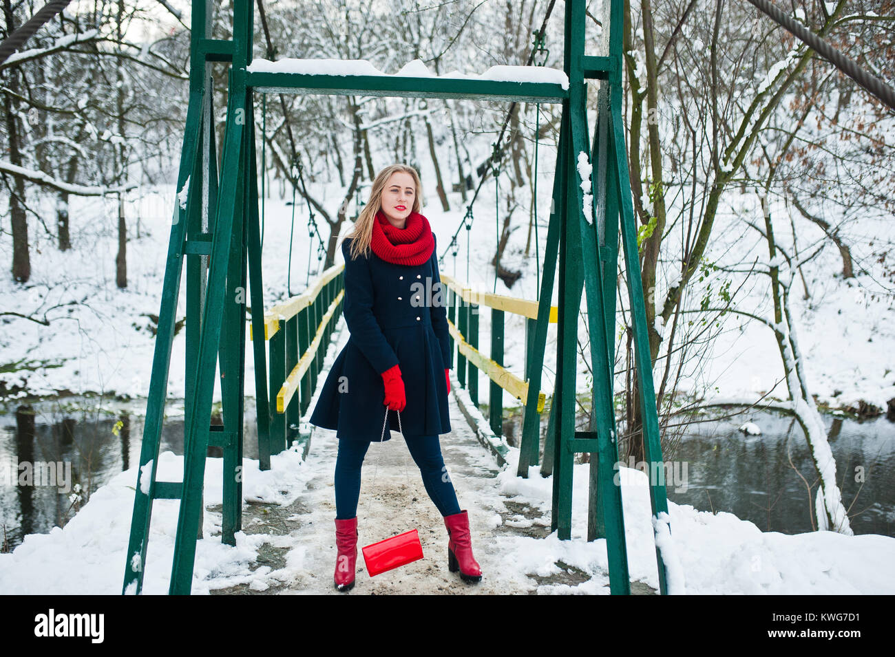 Blonde Mädchen in roten Schal und Mantel zu Fuß über die Brücke im Park im Winter Tag. Stockfoto
