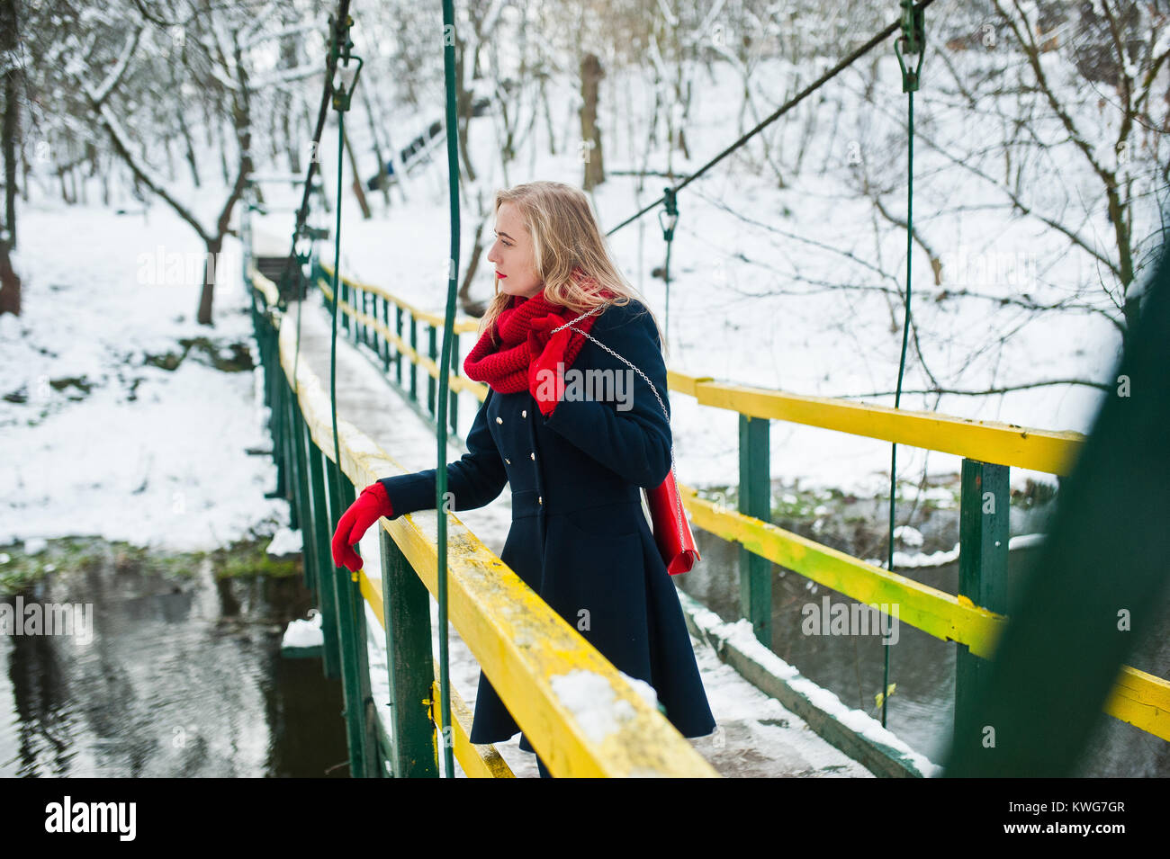 Blonde Mädchen in roten Schal und Mantel zu Fuß über die Brücke im Park im Winter Tag. Stockfoto