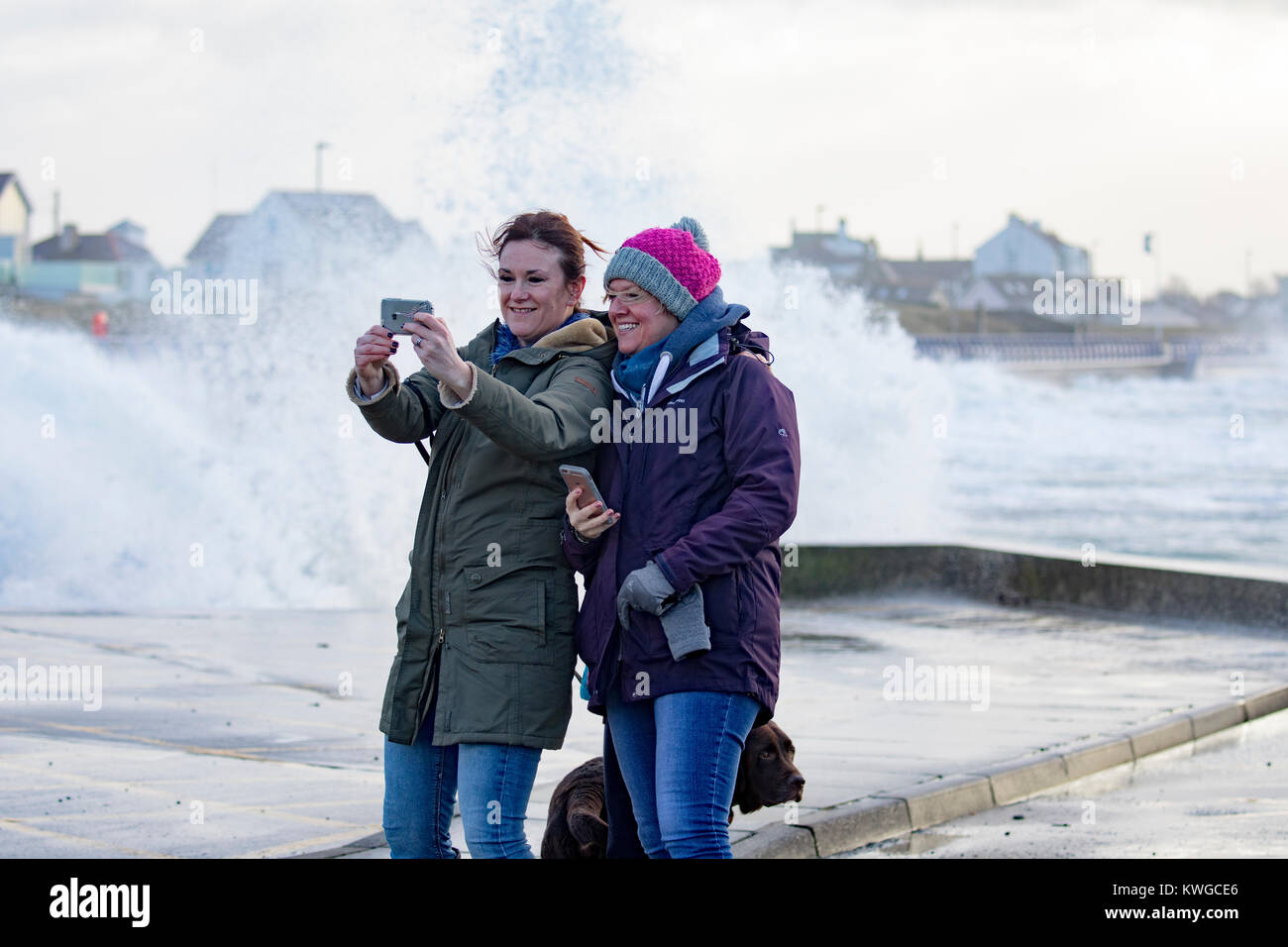 Anglesey, Wales, 3. Januar 2018. UK Wetter. Eine schwere Met Office Warnung hat für das fünfte Sturm der britischen Saison ausgestellt wurde Tropensturm Eleanor. Mit einem Anstieg der Gefahr durch die aktuelle Mond- und Gezeiten Hochwasserwarnungen für viele Bereiche zusammen mit gales Winde wahrscheinlich Schaden zu verursachen. Wellen und Wind Crash in Trearddur Bay auf Anglesey im Norden von Wales, aber immer noch Zeit für eine selfie wie Wellen hinter diese Freunde an der Küste © DGDImages/Alamy leben Nachrichten Stockfoto