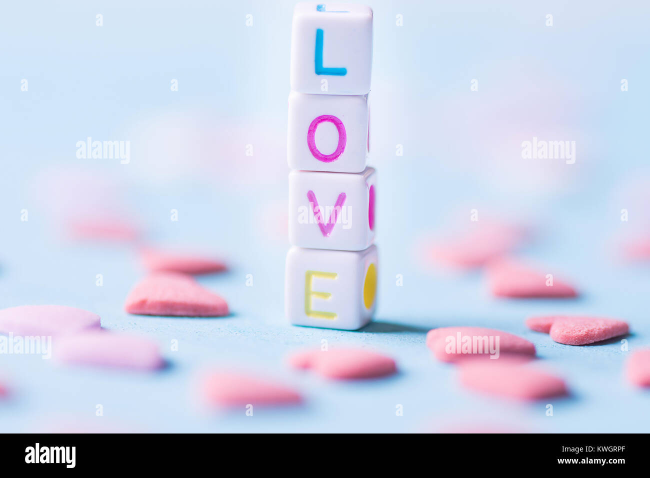 Wort Liebe gebaut aus einzelnen Buchstaben Würfel. Pink Sugar Candy besprüht verstreut auf hellblauem Hintergrund. Romantik Valentinstag Liebe Konzept Stockfoto