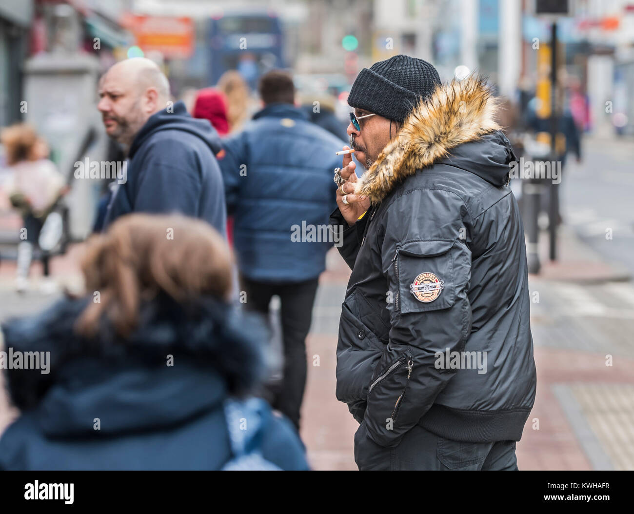 Schwarzer Mann im Winter Kleidung das Rauchen einer Zigarette im Winter in England, UK gekleidet. Stockfoto
