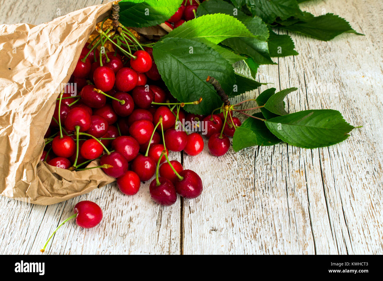 Red Cherry mit Blättern aus einer Papiertüte auf einem weißen Tisch verstreut Reif Stockfoto