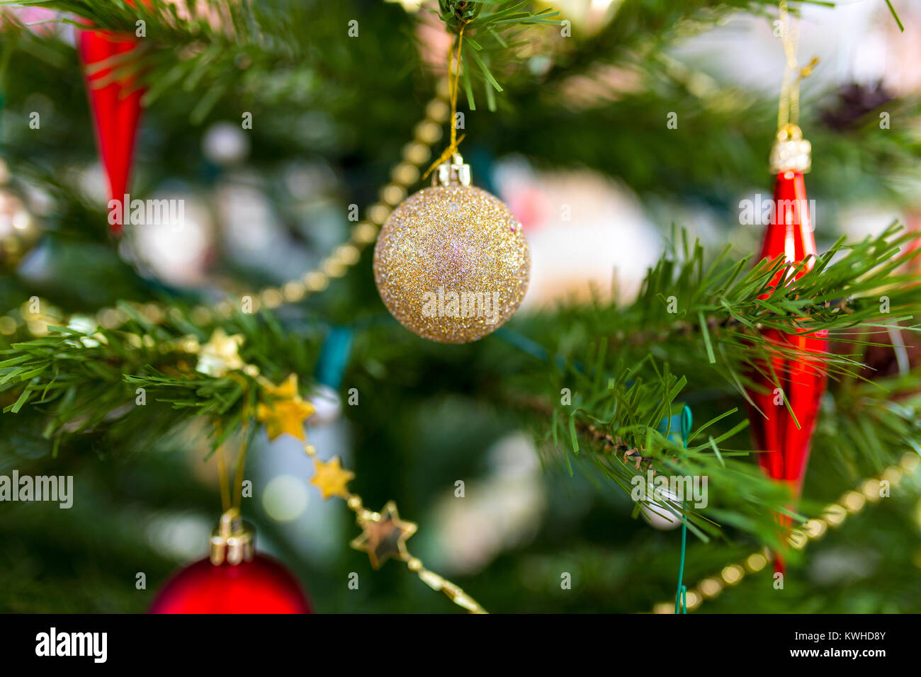 Funkelnde und glänzende gold glitzer Weihnachtskugel hängend auf einer künstlichen festliche Sehr Baum mit goldenen Sternen gewickelt Stockfoto