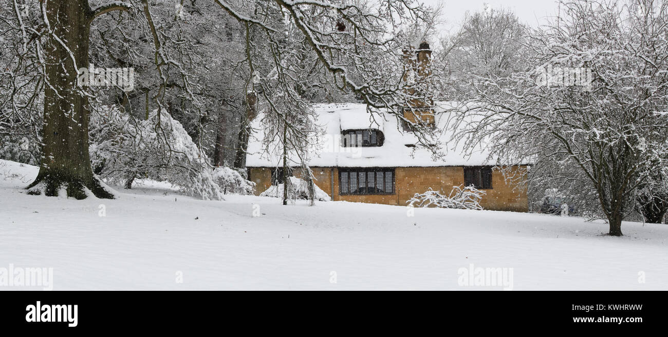 Reetdachhaus und Winter Bäume im Schnee im Dezember bei Batsford Arboretum, Cotswolds, Moreton-in-Marsh, Gloucestershire, England. Panoramablick Stockfoto