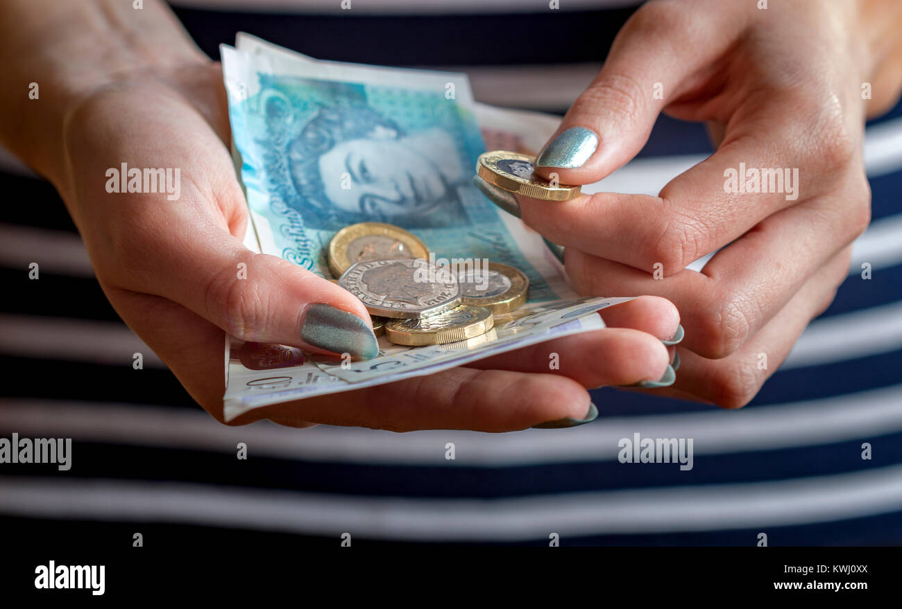 Nahaufnahme der Hände einer Frau mit Bargeld , mit Banknoten und Münzen verschiedener Stückelungen der britischen Währung . Stockfoto