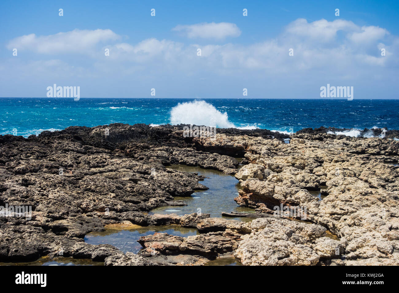 Felsige Küste und Tide Pools mit plätschernden Wellen unter teilweise bewölktem Himmel in Malta. Stockfoto