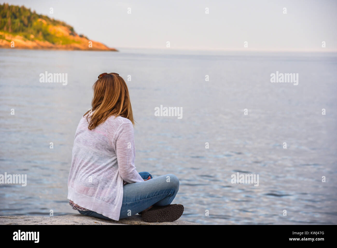 Frau sitzt auf Felsen über den See in Tadoussac, Québec, Kanada Stockfoto
