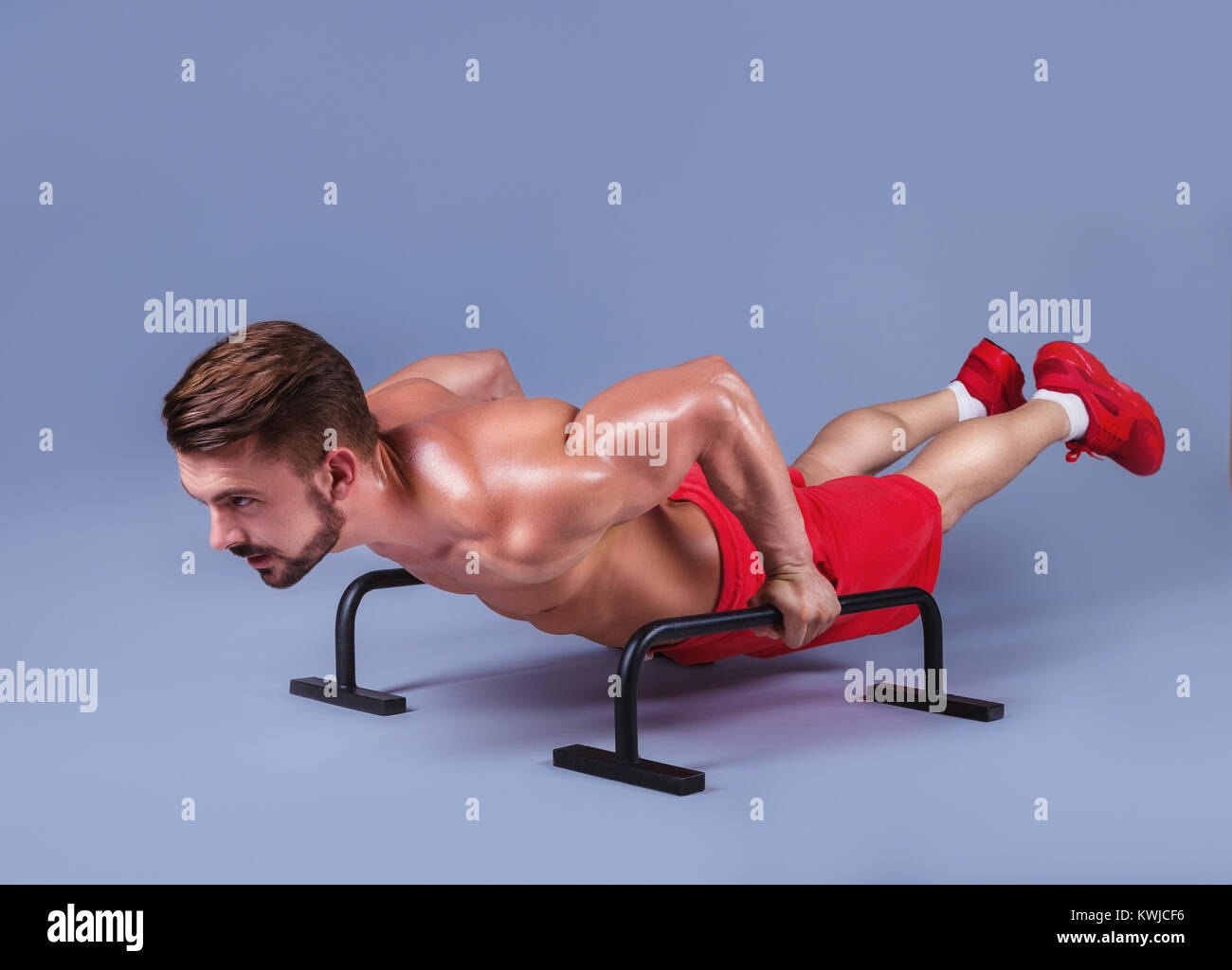 Starken männlichen Athleten zeigt calisthenic bewegt sich längere Beine planche Push-ups auf parallel Bars, Studio shot Stockfoto