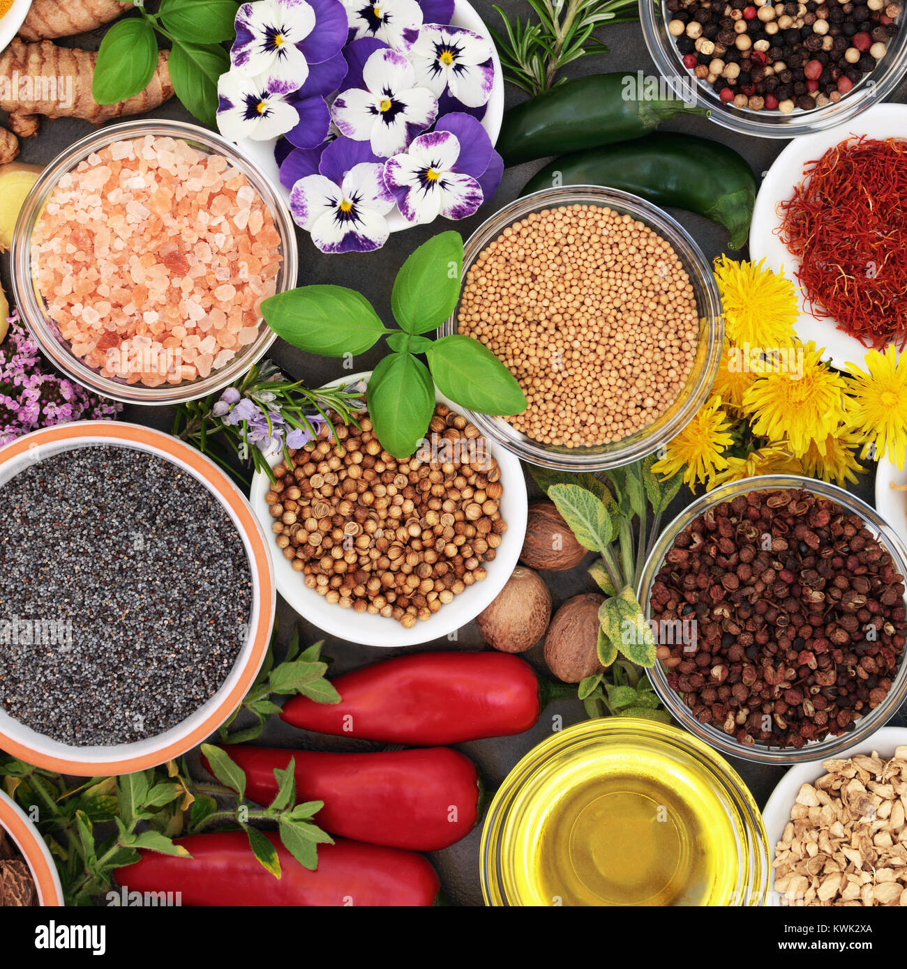 Kräuter und Gewürze mit essbaren frische Blumen und Olivenöl in Schalen und Lose bilden einen bunten Abstrakt Hintergrund. Ansicht von oben. Stockfoto