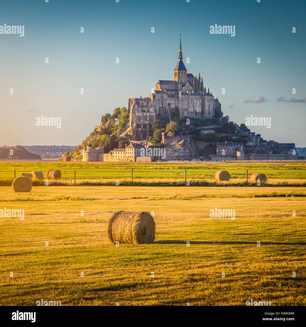 Schöne Aussicht von berühmten historischen Le Mont Saint-Michel im goldenen Abendlicht bei Sonnenuntergang im Sommer mit Heuballen auf Feldern, Normandie, Frankreich Stockfoto
