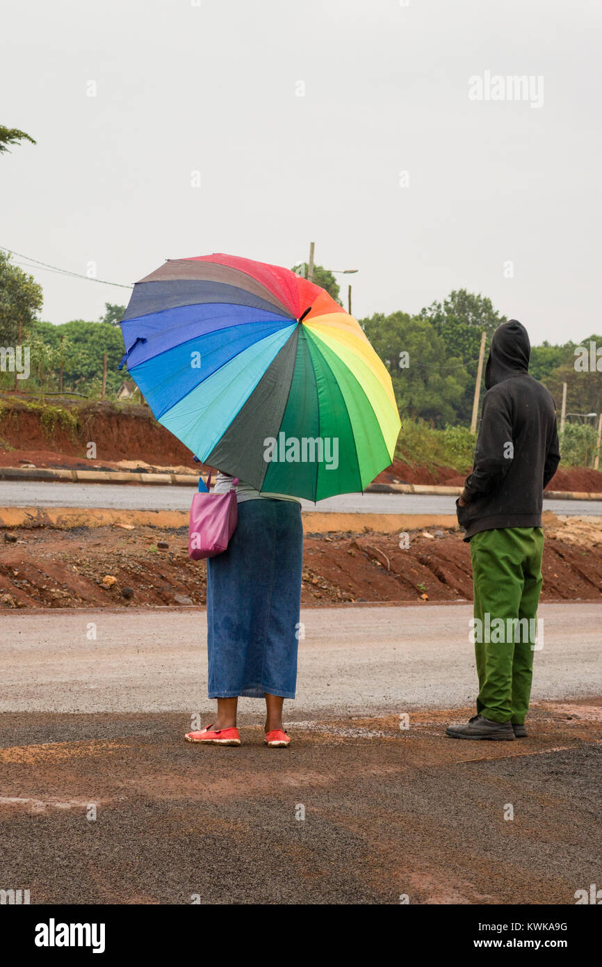 Eine kenianische Frau mit Sonnenschirm steht im Regen am Straßenrand, Nairobi, Kenia Stockfoto