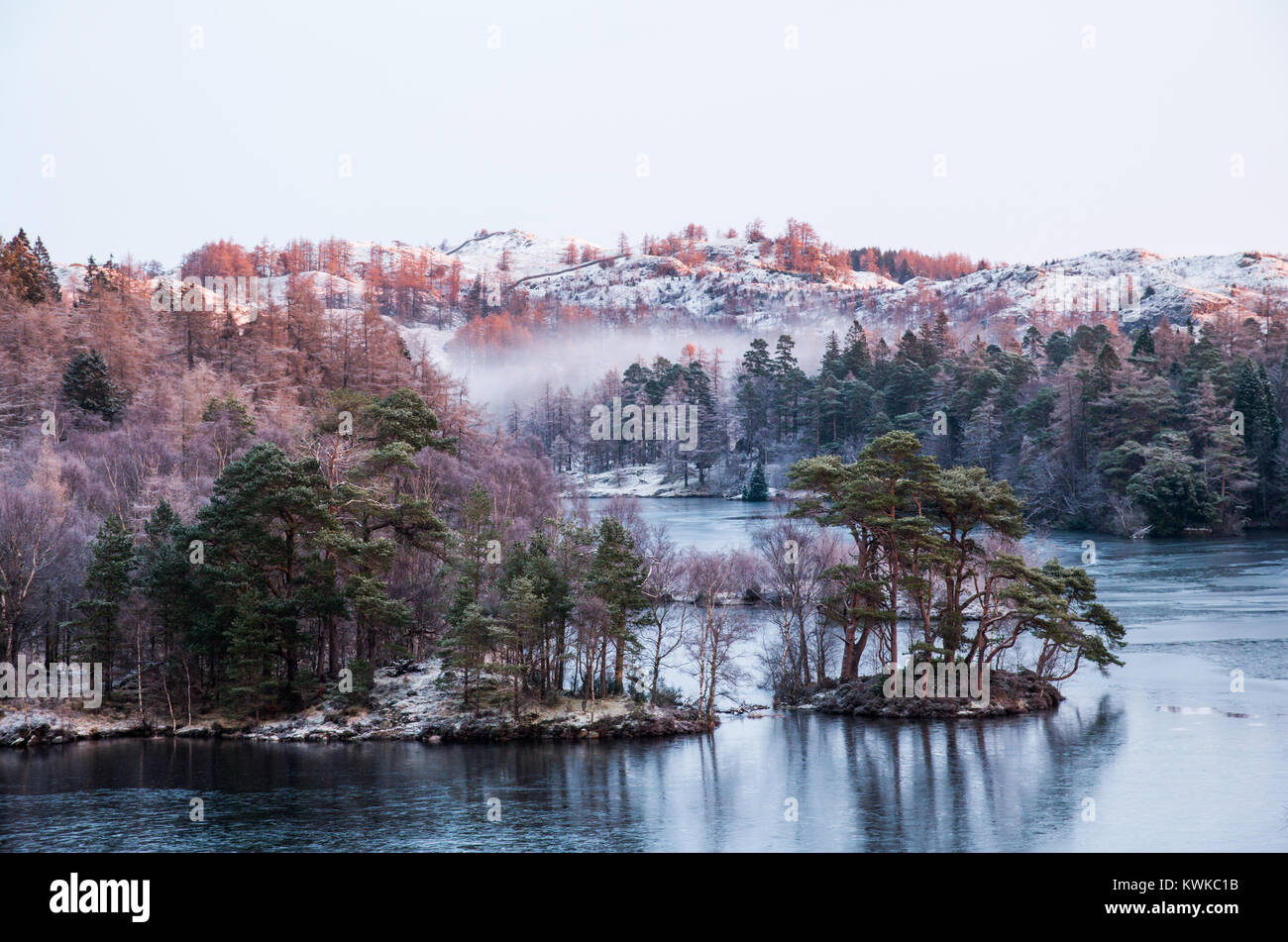 Eine morgendliche Szene auf Tarn Hows See mit Sonnenlicht schlagen der Frost bedeckte Hügel und Nebel in den niederen Bereichen. Stockfoto