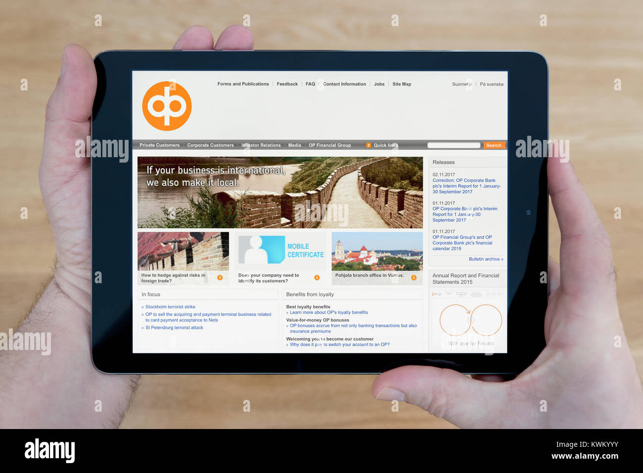 Ein Mann schaut auf die OP Financial Group - Pohjola Website auf seinem iPad Tablet Vorrichtung, die auf einer hölzernen Tisch top Hintergrund (nur redaktionelle Nutzung) Stockfoto