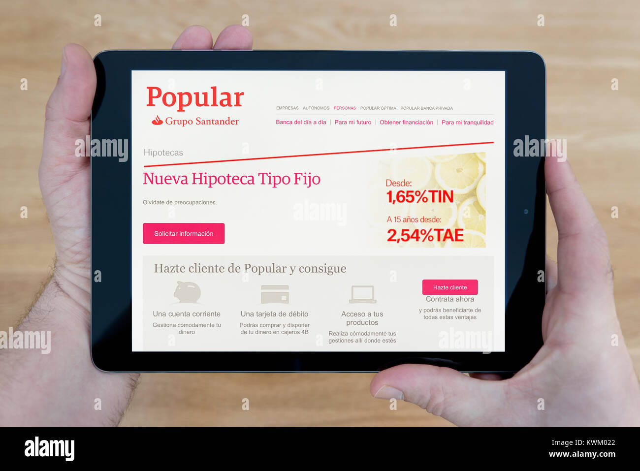 Ein Mann schaut auf die Banco Popular Website auf seinem iPad Tablet Vorrichtung, die auf einer hölzernen Tisch top Hintergrund (nur redaktionelle Nutzung) Stockfoto