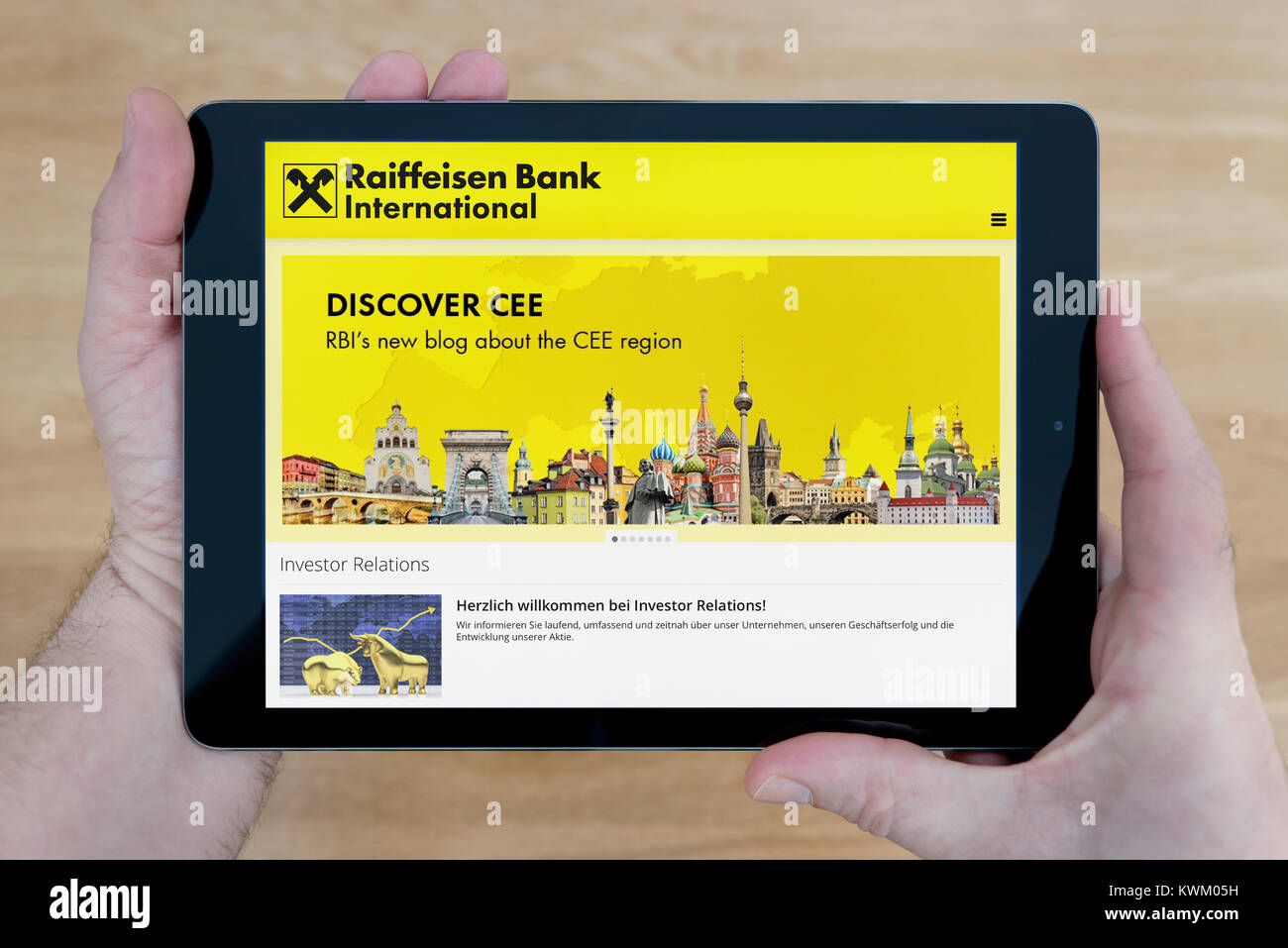 Ein Mann schaut auf die RBI (Raiffeisen Bank International) website auf seinem iPad Tablet Vorrichtung, die auf einer hölzernen Tisch top Hintergrund (nur redaktionelle Nutzung) Stockfoto