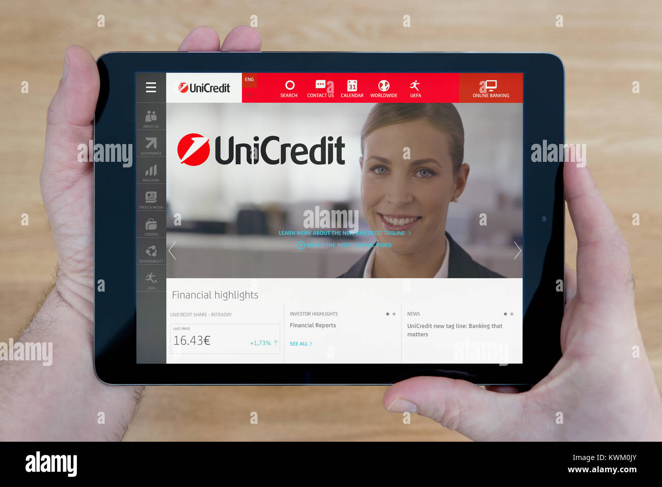 Ein Mann schaut sich die UniCredit Bank Website auf seinem iPad Tablet Vorrichtung, die auf einer hölzernen Tisch top Hintergrund (nur redaktionelle Nutzung) Stockfoto