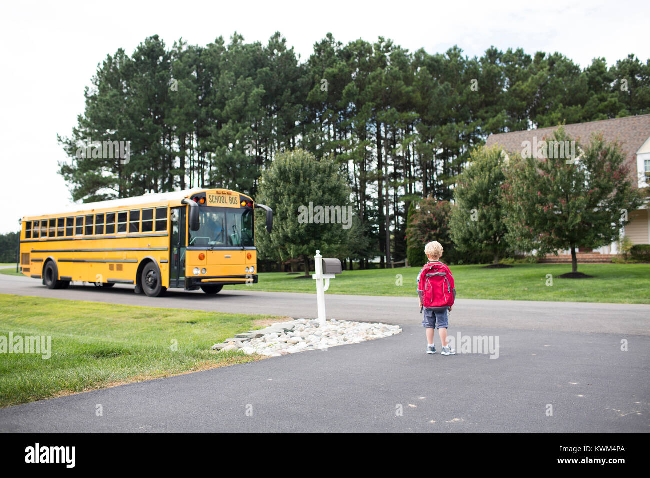 Ansicht der Rückseite des Jungen mit Rucksack warten auf Schulbus auf der Straße Stockfoto