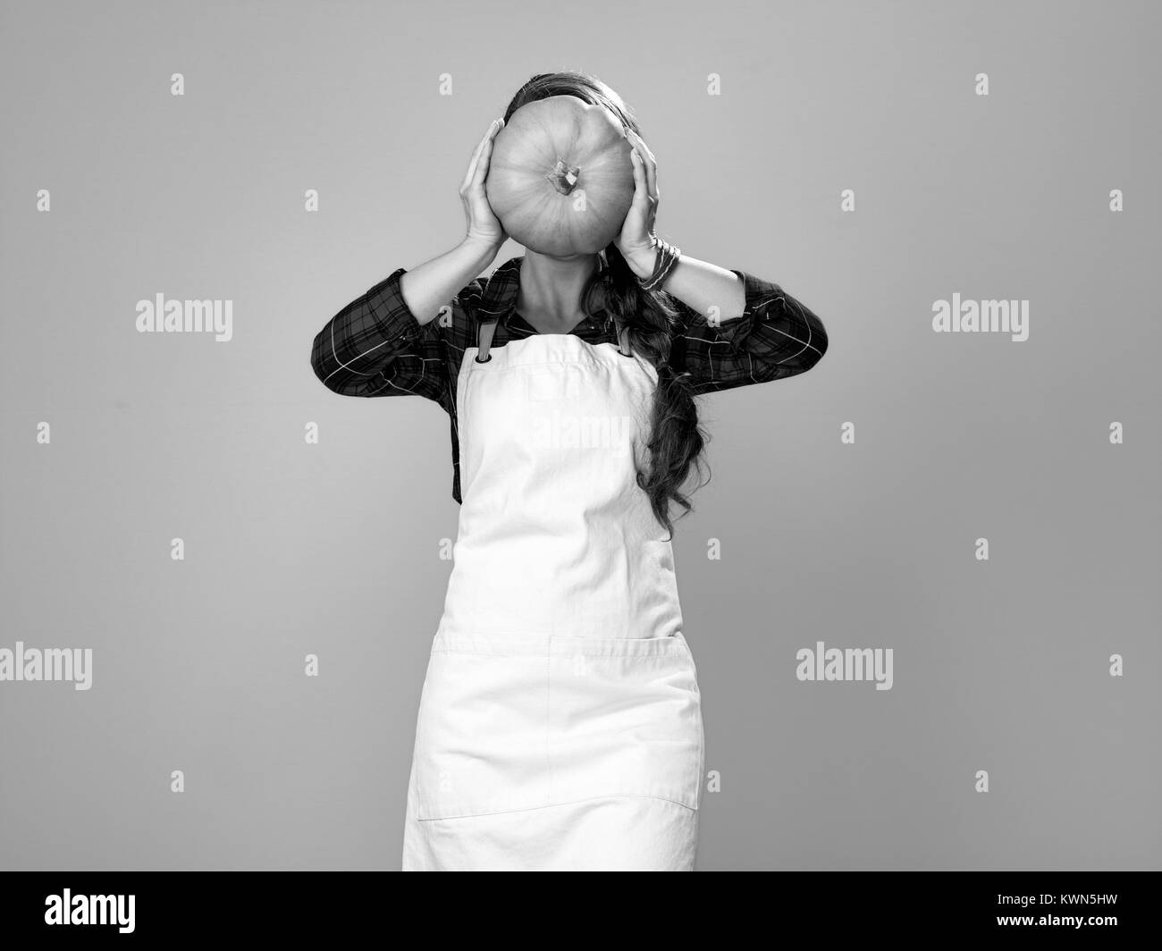 Gesundes Essen auf den Tisch. moderne Frau Bauer tragen Schürze auf gelbem Hintergrund holding Kürbis in der Vorderseite des Gesicht Stockfoto