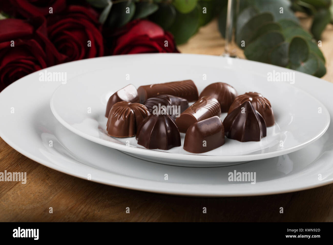 Platte von Pralinen schließen oben mit Rosen im Hintergrund Stockfoto