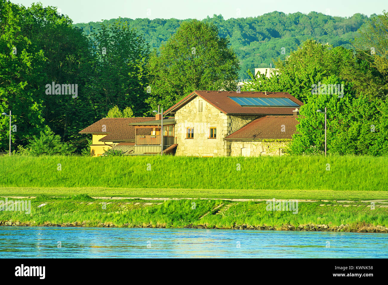 Blick auf die Donau Bank der Donaupark Linz Oberösterreich. Leuchtende grüne Farbe, goldenes Sonnenlicht Bergpanorama im Hintergrund. Sommer Spri Stockfoto