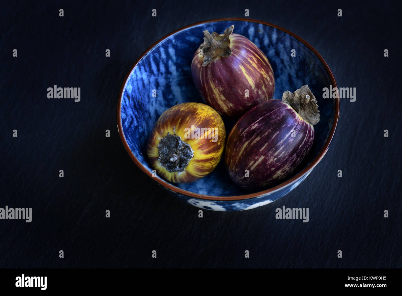 Gesunde und frische lila Auberginen in einem bwols über dunklen Stein Hintergrund. Vegetarische Ernährung, Gesundheit oder Kochen Konzept, Ansicht von oben, kopieren Raum Stockfoto