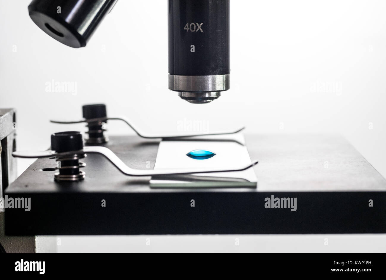Mikroskop und Mikroskop Objektträger closeup, hinterleuchtet, Makro, mit einem kleinen blauen Stoff liquid Droplet auf dem Objektträger, weißer Hintergrund Stockfoto
