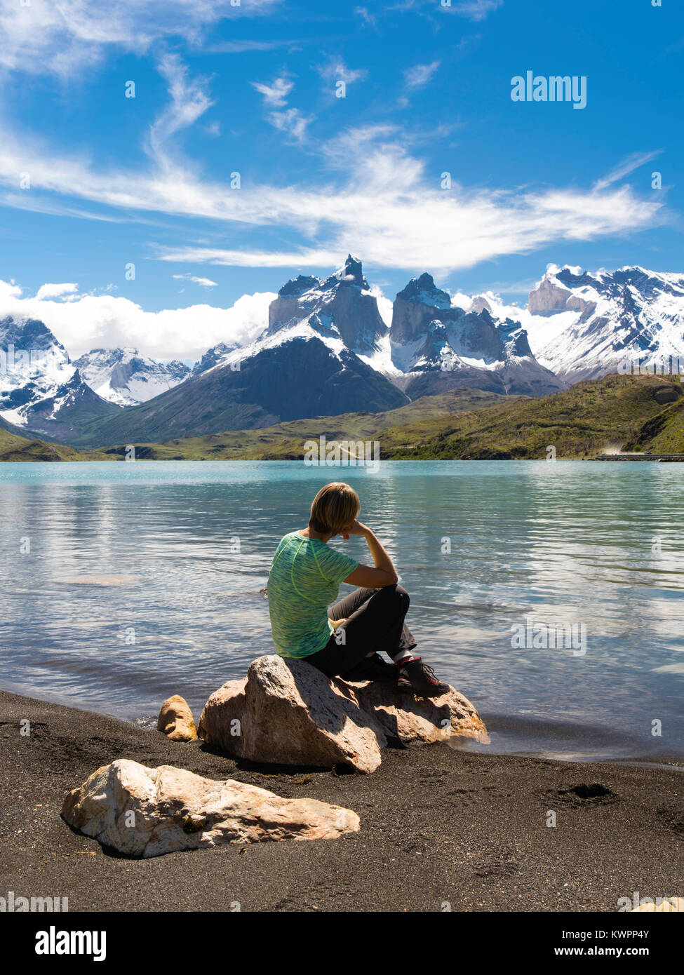 Eine Frau sitzt auf einem Felsen und genießt die Aussicht auf Cuerno Kapitalbetrag über Lago Pehoe, Torres del Paine Nationalpark, Chile. Stockfoto