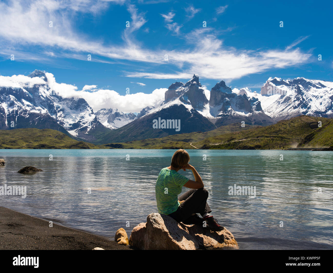 Eine Frau sitzt auf einem Felsen und genießt die Aussicht auf Cuerno Kapitalbetrag über Lago Pehoe, Torres del Paine Nationalpark, Chile. Stockfoto