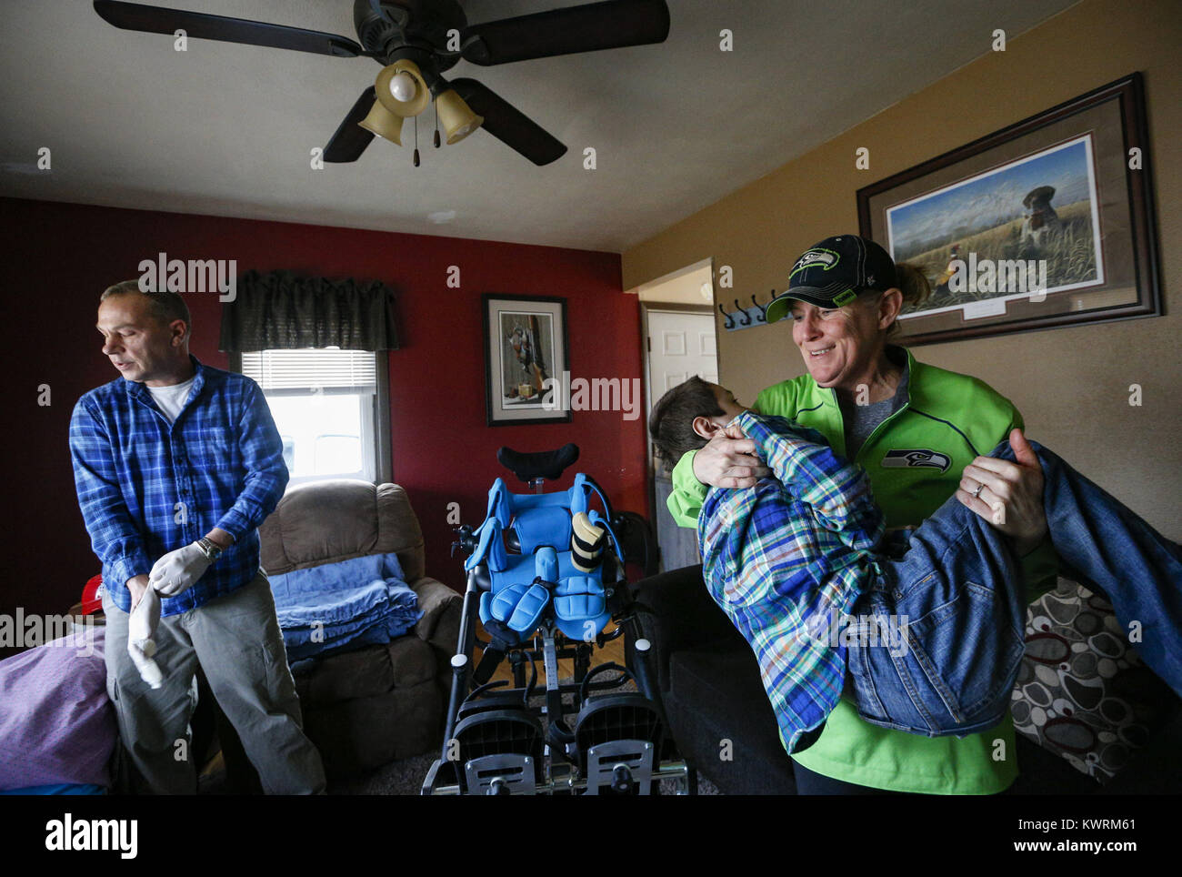 Davenport, Iowa, USA. 12. Januar 2017. Tina McDermott hebt Sohn, Ryan, 10, auf der Couch für Randy Cox, eine examinierte Krankenschwester mit Einheit Punkt Kinderheilkunde, der vier Jahre Arbeit mit Ryan zu Hause in Davenport McDermott auf Donnerstag, 12. Januar 2017 verbracht hat. McDermott war als Kleinkind mit Dravet-Syndrom, einer schweren Form von Epilepsie diagnostiziert und hat derzeit zwischen 10 und 20 Anfälle pro Tag. Eine Cannabis-Öl-Studie durch die Universität von Iowa funktionierte nicht für McDermott, aber er wird in Kürze eine Studie durch die Mayo-Klinik namens Fenfluramin Bewertung bei seltenen Epilepsie beginnen. (Kredit Im Stockfoto