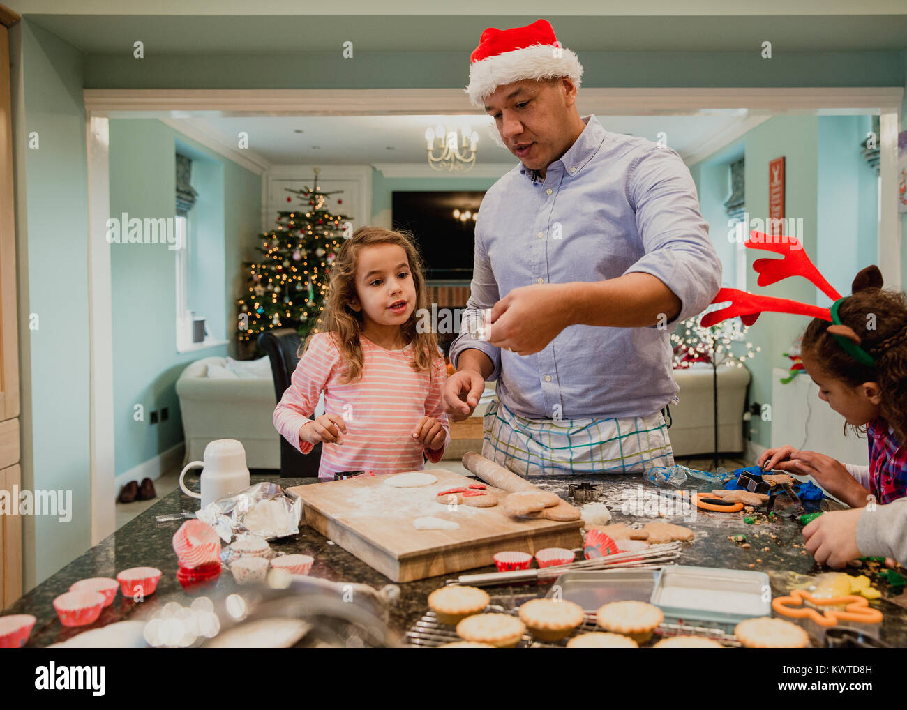 Kleine Mädchen machen Weihnachten Kekse zu Hause mit ihrem Vater. Ihre Mutter ist gerade diese Form der Esstisch, wo Sie arbeitet. Stockfoto