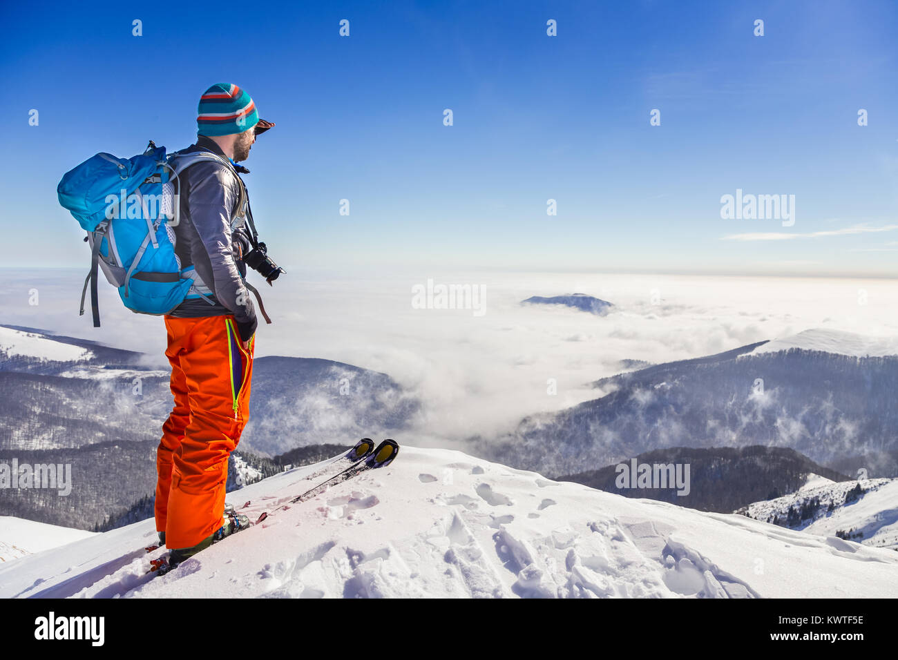 Jungen kaukasischen Mann genießen Sie den Blick auf das Tal von einem Grat beim Skifahren in frischem Schnee an einem sonnigen Tag Stockfoto
