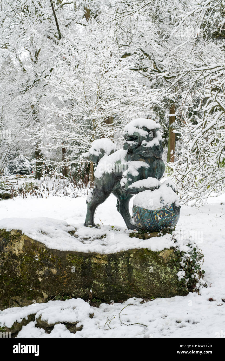 Chinese Foo Dog Bronzestatue und Winter Bäume im Schnee im Dezember bei Batsford Arboretum, Cotswolds, Moreton-in-Marsh, Gloucestershire, England Stockfoto