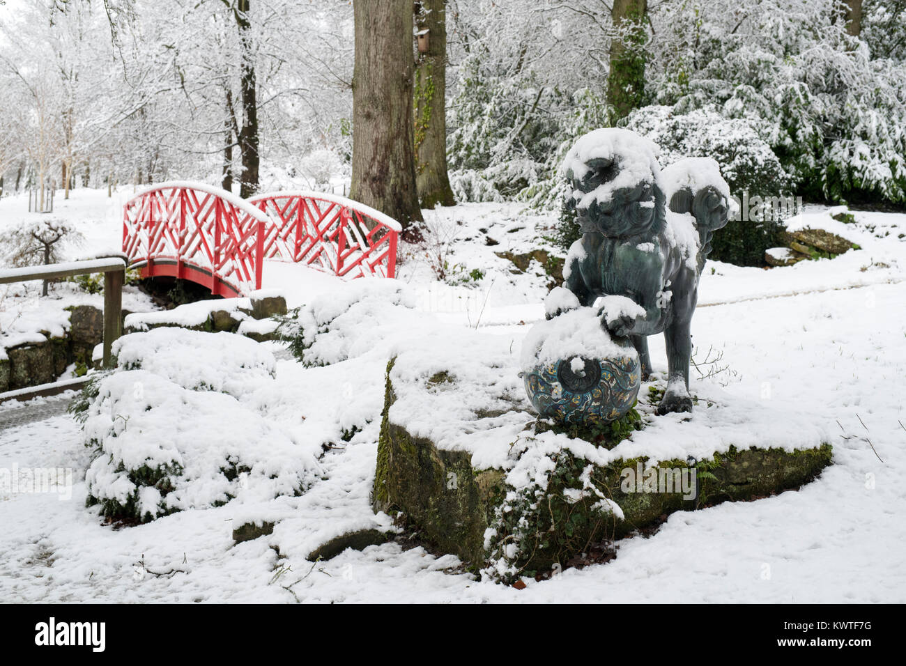 Chinese Foo Dog Bronzestatue und japanische Brücke im Schnee im Dezember bei Batsford Arboretum, Cotswolds, Moreton-in-Marsh, Gloucestershire, England Stockfoto