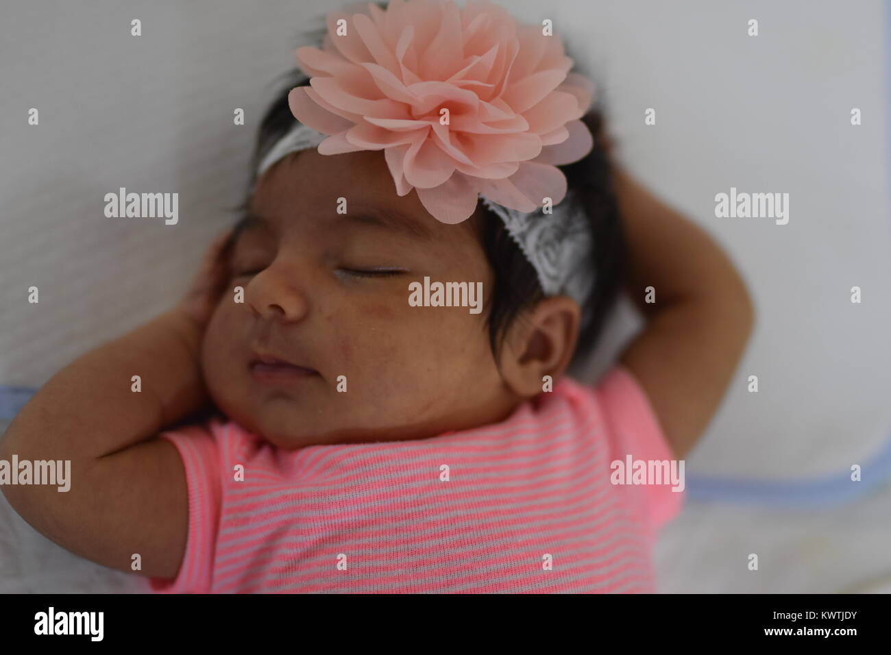 Neugeborenes Mädchen in rosa schläft friedlich auf dem Rücken, mit den Armen um den Kopf Stockfoto