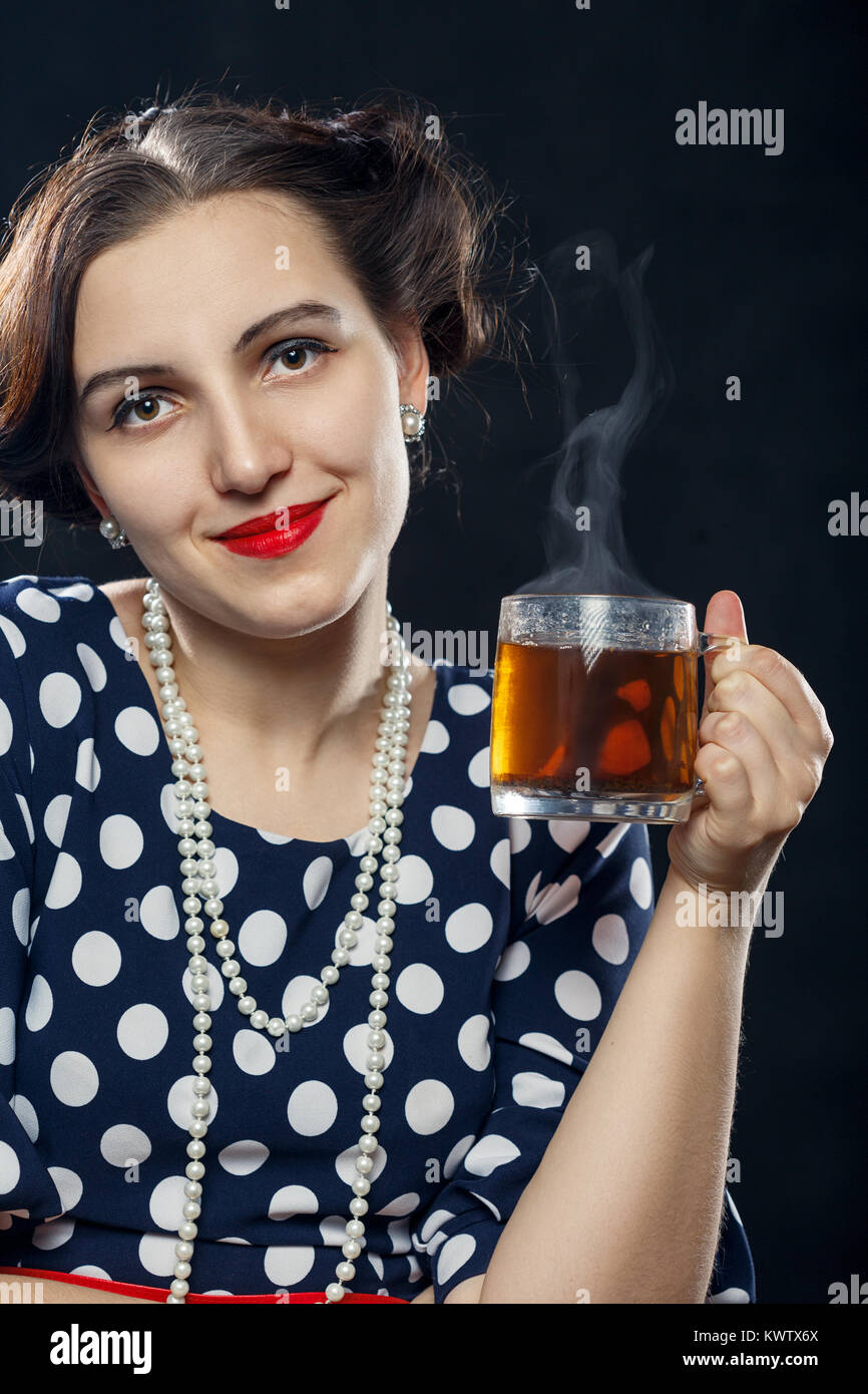 Schöne pinup Frau mit einer Tasse Tee auf schwarzem Hintergrund in die Kamera lächeln Stockfoto