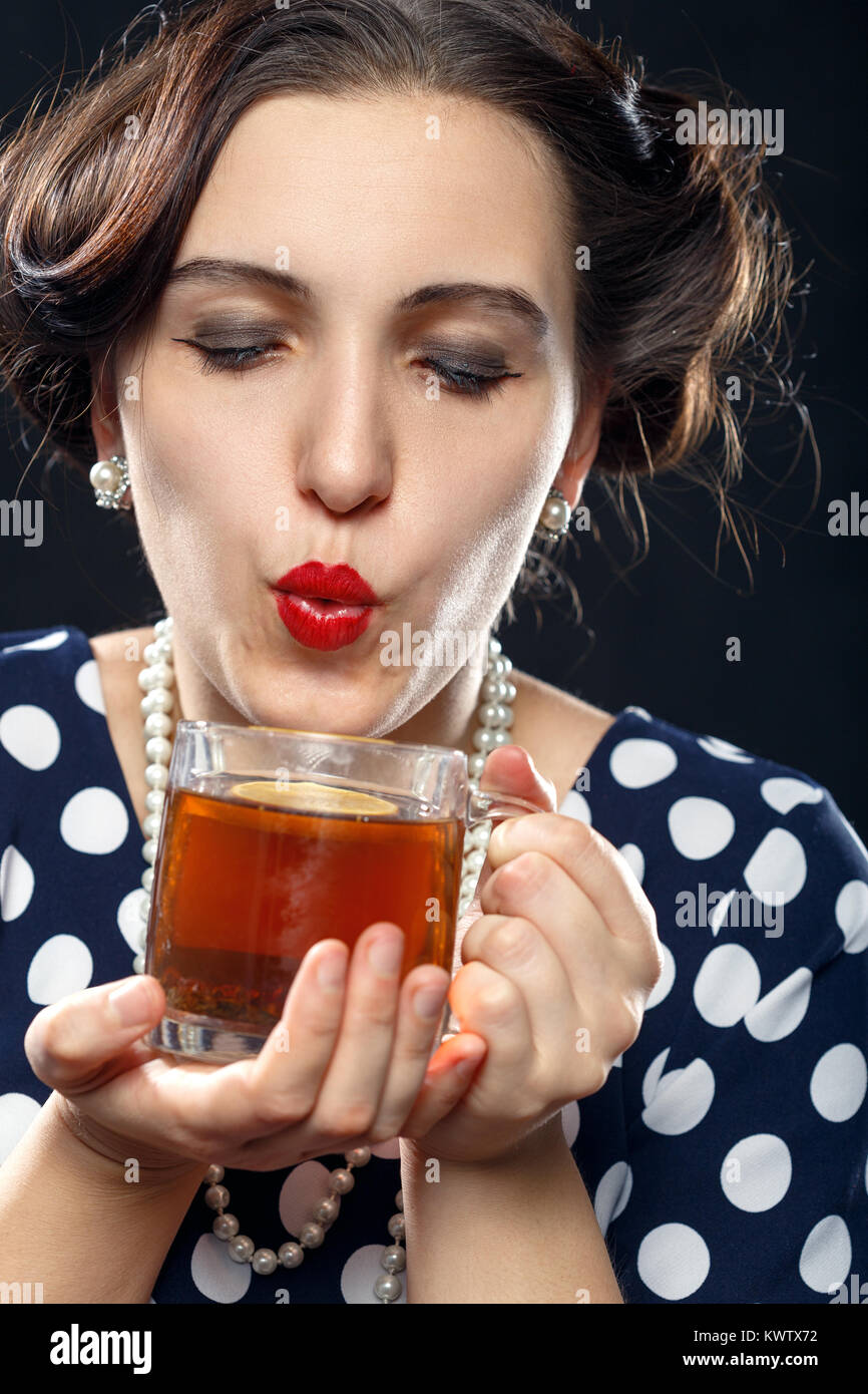 Schöne pinup Frau mit Tasse Tee auf schwarzen Hintergrund an Kamera blow suchen Stockfoto