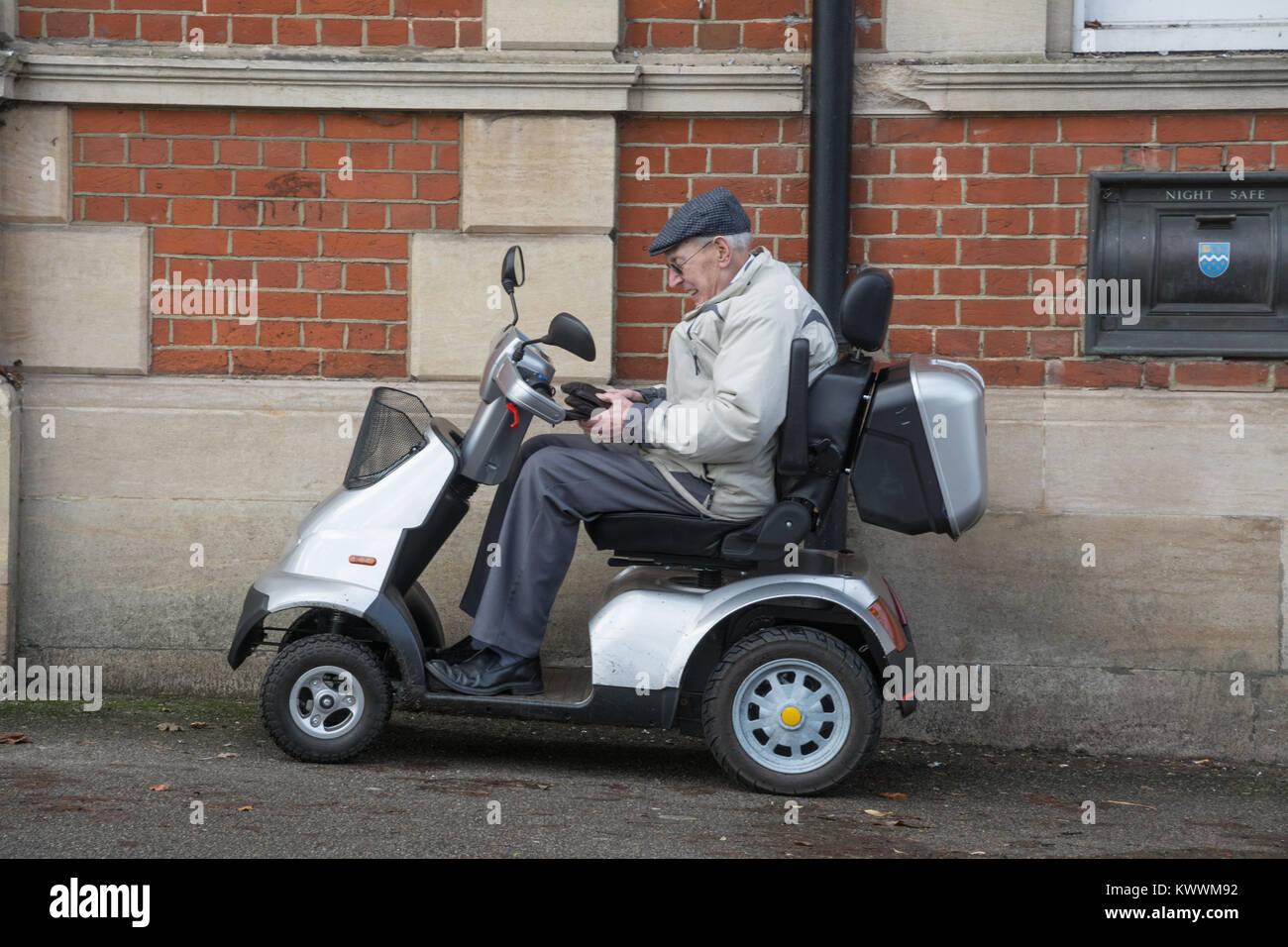Ältere Mann sitzt auf einem Mobility Scooter außerhalb einer Bank Stockfoto